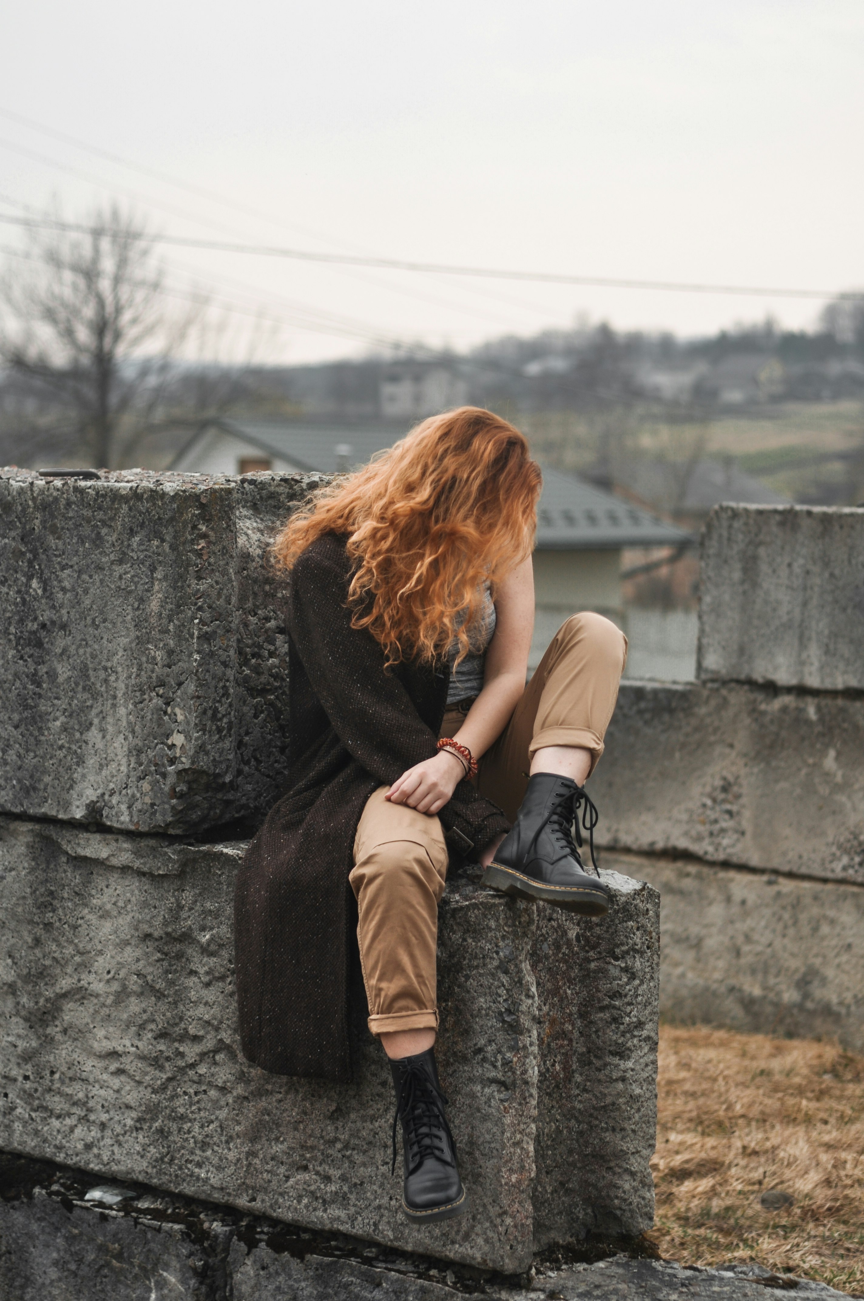 woman in brown long sleeve shirt and brown pants sitting on gray concrete wall during daytime